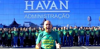 luciano hang fala para a câmera com funcionários uniformizados atrás em frente à uma loja da havan