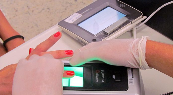 pessoa usando luvas segura nas mãos de uma mulher para cadastrar o dedo em um leitor de digitais