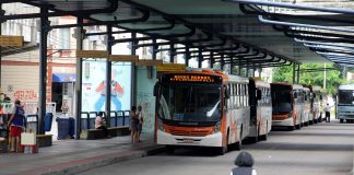 mulher caminha em direção a plataforma do terminal, onde há dois ônibus estacionados