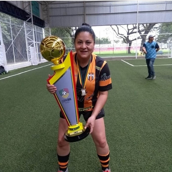 thay posa para a câmera segurando taça e usando uniforme em uma quadra de grama sintética