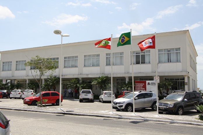 fachada do prédio da camara com alguns carros estacionados à frente e bandeiras hasteadas