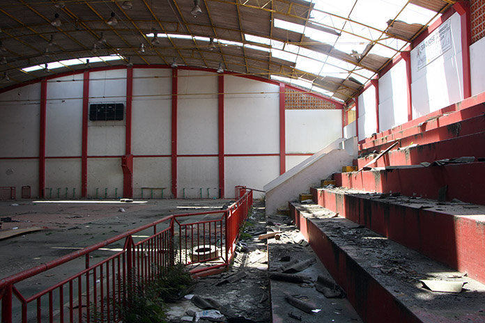 parte interior do ginásio cheia de lixos e detritos e mostrando o teto todo quebrado e cheio de buracos