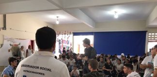 homem visto de costas com camisa escrita "observador social" fala para um grupo de estudantes