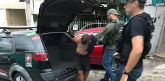 homem preso é retirado algemado da viatura por dois agentes armados
