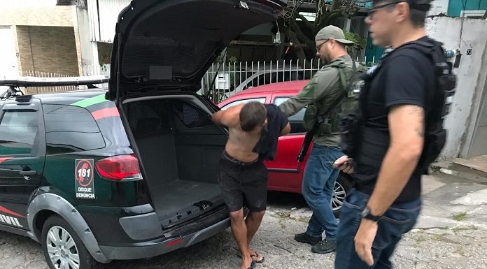 homem preso é retirado algemado da viatura por dois agentes armados