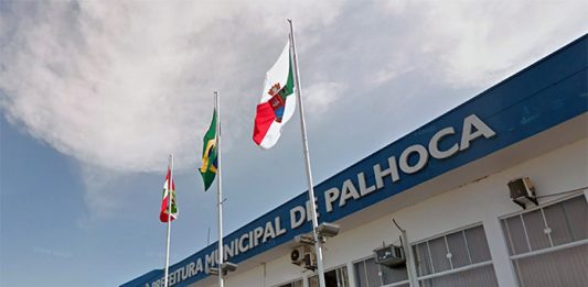 Prefeito de Palhoça anuncia aquisição da sede administrativa da prefeitura fachada do prédio atual da prefeitura de palhoça com as bandeira de sc, br e do município à frente