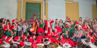 coral natalino vestido à caráter com um papai noel no meio com os braços pra cima em frente à igreja matriz de sj