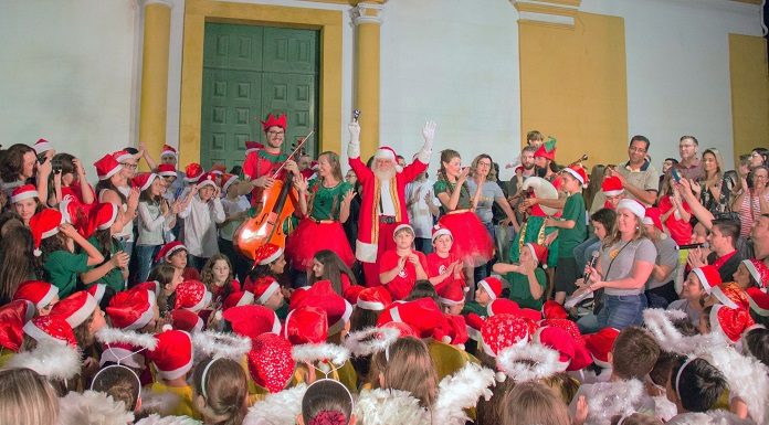 coral natalino vestido à caráter com um papai noel no meio com os braços pra cima em frente à igreja matriz de sj