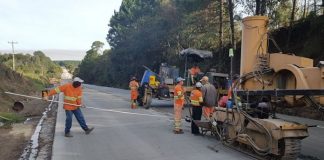 trabalhadores uniformaizado em rodovia recém asfaltada ao lado de grande máquina em área rural
