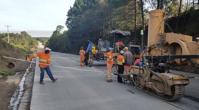 trabalhadores uniformaizado em rodovia recém asfaltada ao lado de grande máquina em área rural