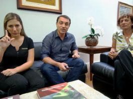 Decreto regulamentará uso do nome social nos serviços públicos estaduais governador falando para a câmera, sentado em um sofá ao lado de uma intérprete em libras e de um homem trans
