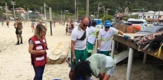 três pessoas conversam com morador de rua deitado em areia de praia