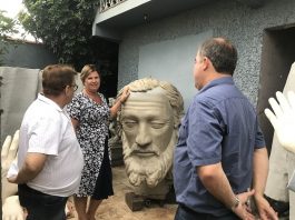 prefeita adeliana apoiada na cabeça da estátua, que é quase do seu tamanho, conversando com dois homens