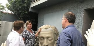 prefeita adeliana apoiada na cabeça da estátua, que é quase do seu tamanho, conversando com dois homens