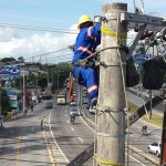 dois operários com equipamentos de proteção trabalham em ligação da rede elétrica no alto de um poste