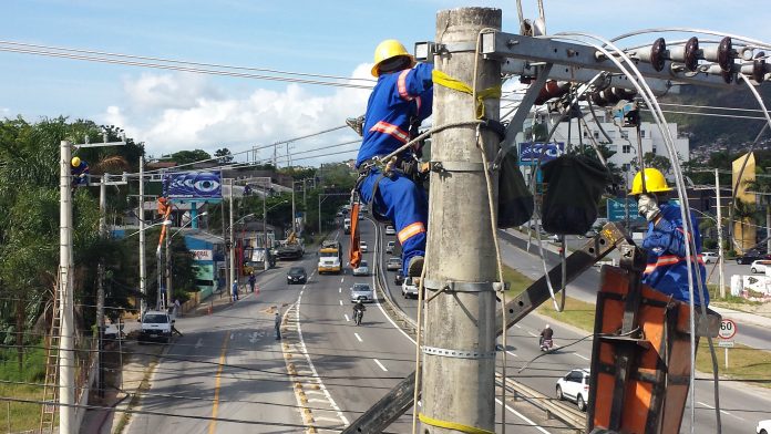 dois operários com equipamentos de proteção trabalham em ligação da rede elétrica no alto de um poste