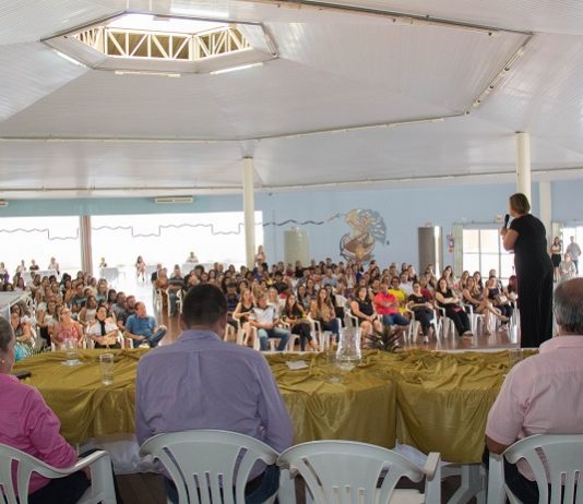 prefeita adeliana vista por detrás do palco onde há pessoas sentadas falando com a grande plateia ao fundo