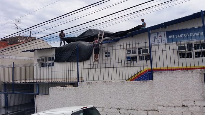 dois homens colocam lonas sobre o posto de saúde