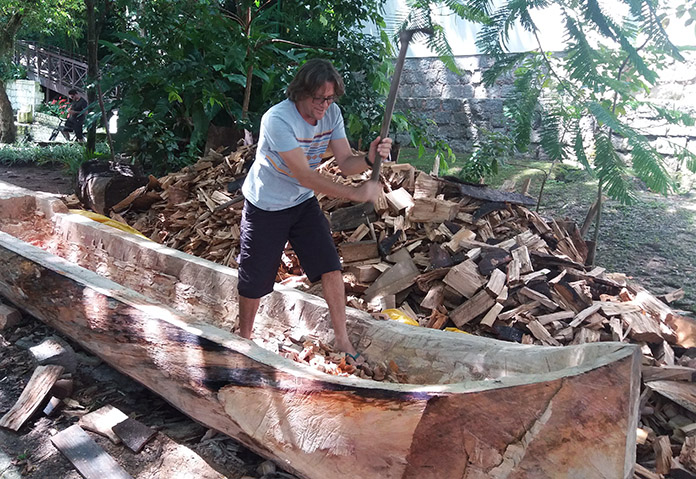 lourival dentro da canoa com uma ferramenta de enxó levantada pronto para dar um golpe na madeira
