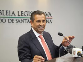 Por unanimidade, Julio Garcia assume pela terceira vez a presidência da Alesc deputado fala sorridente ao microfone em bancada e atrás na parede logo da alesc