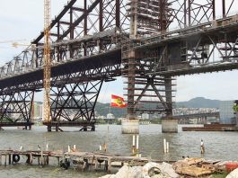 close na estrutura da ponte hercílio luz com uma bandeira de sc tremulando à frente