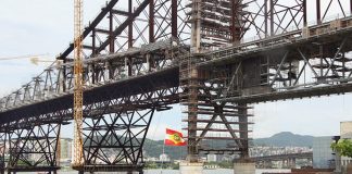 close na estrutura da ponte hercílio luz com uma bandeira de sc tremulando à frente