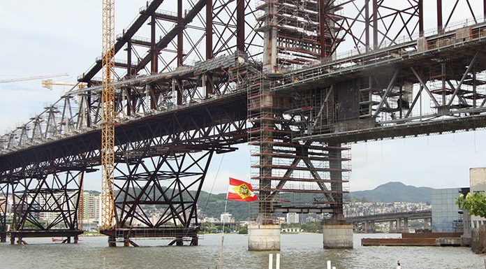 close na estrutura da ponte hercílio luz com uma bandeira de sc tremulando à frente
