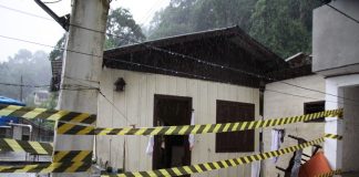 foto de uma casa onde houve desabamento e morte com uma fita zebrada na frente e chovendo