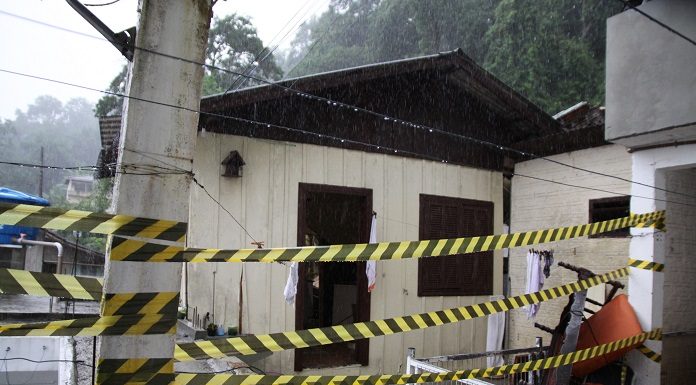 foto de uma casa onde houve desabamento e morte com uma fita zebrada na frente e chovendo