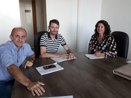 os dois vereadores e a vereadora sentados na ponta de uma mesa em uma sala olham para a câmera