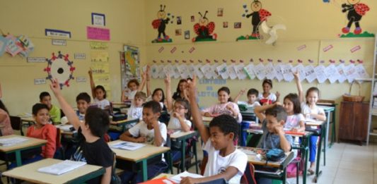 crianças uniformizadas em uma sala de aula com os braços levantados