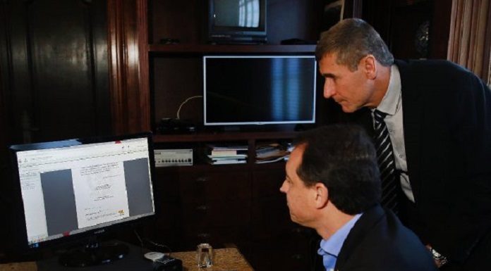 governador mexe no computador e secretario ao lado olhando para a tela