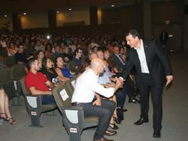 Rede estadual de ensino recebe 911 novos professores governador se inclina para cumprimentar homem sentado em poltrona do teatro, lotado de docentes