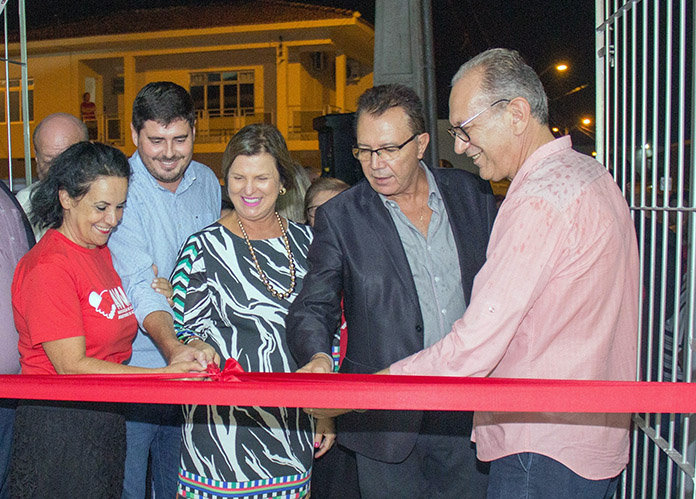 as cinco pessoas seguram a faixa vermelha de inauguração na porta