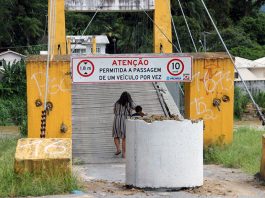 mulher carrega bicicleta andando para entrar na ponte, que tem uma tubulação de concreto colocada na frente para marcar a interdição