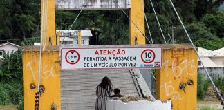 mulher carrega bicicleta andando para entrar na ponte, que tem uma tubulação de concreto colocada na frente para marcar a interdição