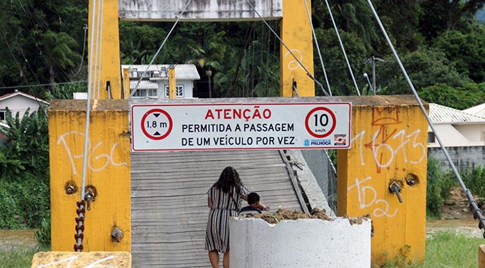 mulher carrega bicicleta andando para entrar na ponte, que tem uma tubulação de concreto colocada na frente para marcar a interdição