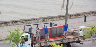 trabalhadores em cima de um caminhão colocam placa sobre um ponto de ônibus em uma avenida com coqueiros