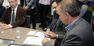 prefeito gean assina documento na ponta de uma mesa cercado de gente