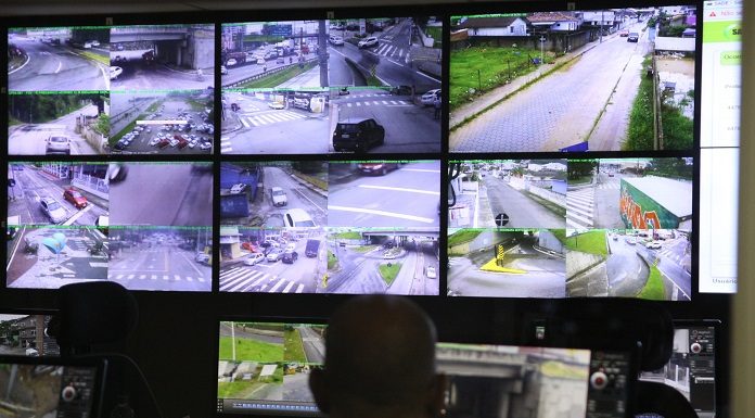 homem olhando um painel com diversas telas de cameras de ruas na central de videomonitoramento