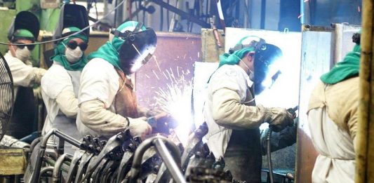 Taxa de desemprego volta a crescer depois de duas quedas consecutivas operários de solda trabalhando e outros olhando para a câmera