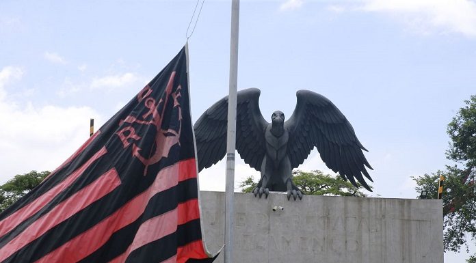 bandeira do flamengo à meio mastro em frente a uma estátua de um urubu
