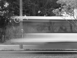 imagem em preto e branco e borrada de um ônibus passando em velocidade em frente a uma bicicleta fantasma