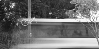 imagem em preto e branco e borrada de um ônibus passando em velocidade em frente a uma bicicleta fantasma