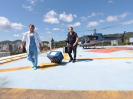 médico carrega caixa térmica por um heliponto no alto de um prédio em balneário camboriú; helicóptero ao fundo e outro homem
