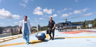 médico carrega caixa térmica por um heliponto no alto de um prédio em balneário camboriú; helicóptero ao fundo e outro homem