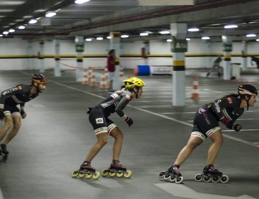 três patinadoras disputam corrida em um estacionamento coberto