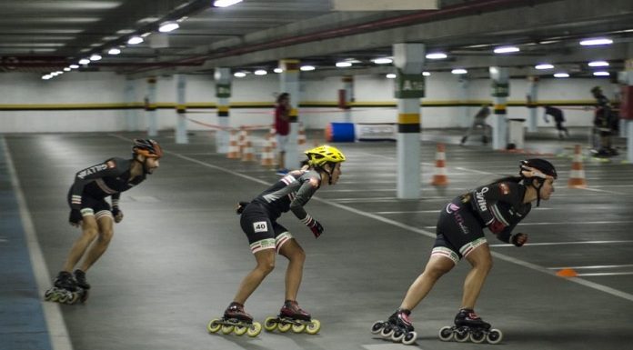 três patinadoras disputam corrida em um estacionamento coberto
