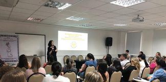 enfermeira soninha em pé dando a palestra para uma sala cheia