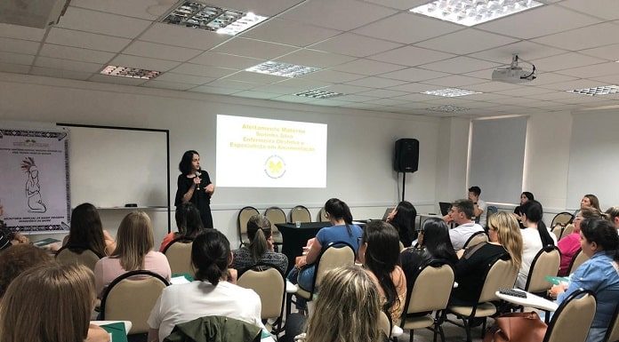 enfermeira soninha em pé dando a palestra para uma sala cheia